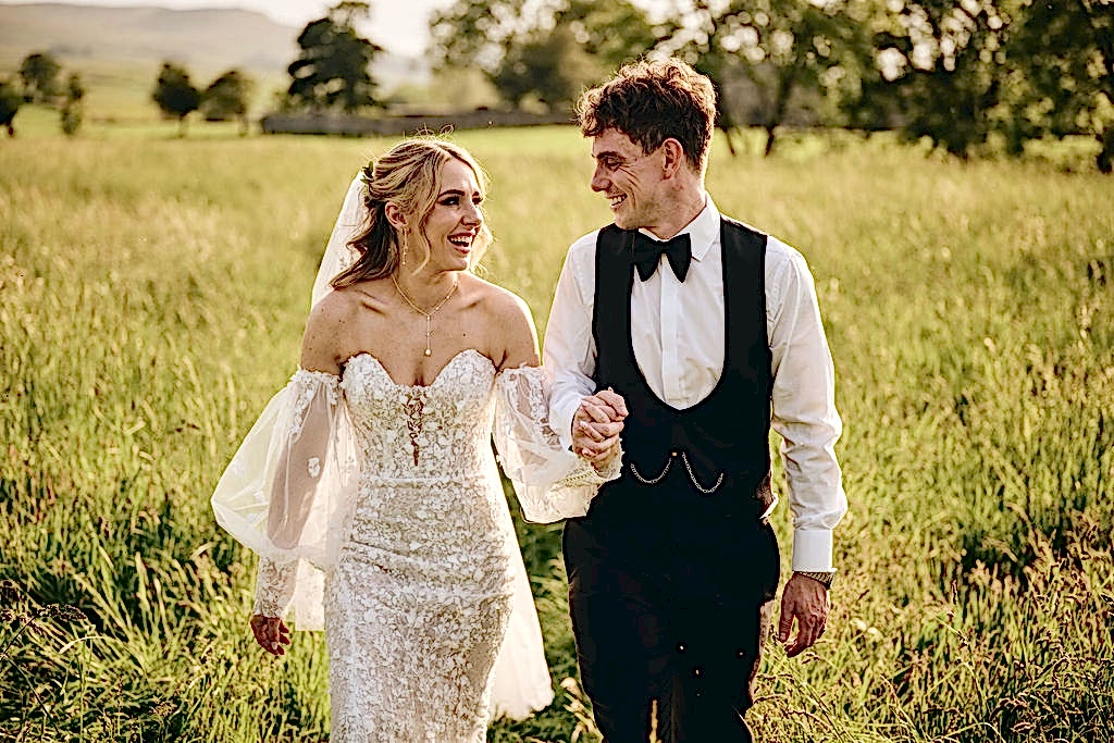 The image shows Poppy and Tom (the bride and groom) walking hand in hand through the countryside at Yorebridge House.