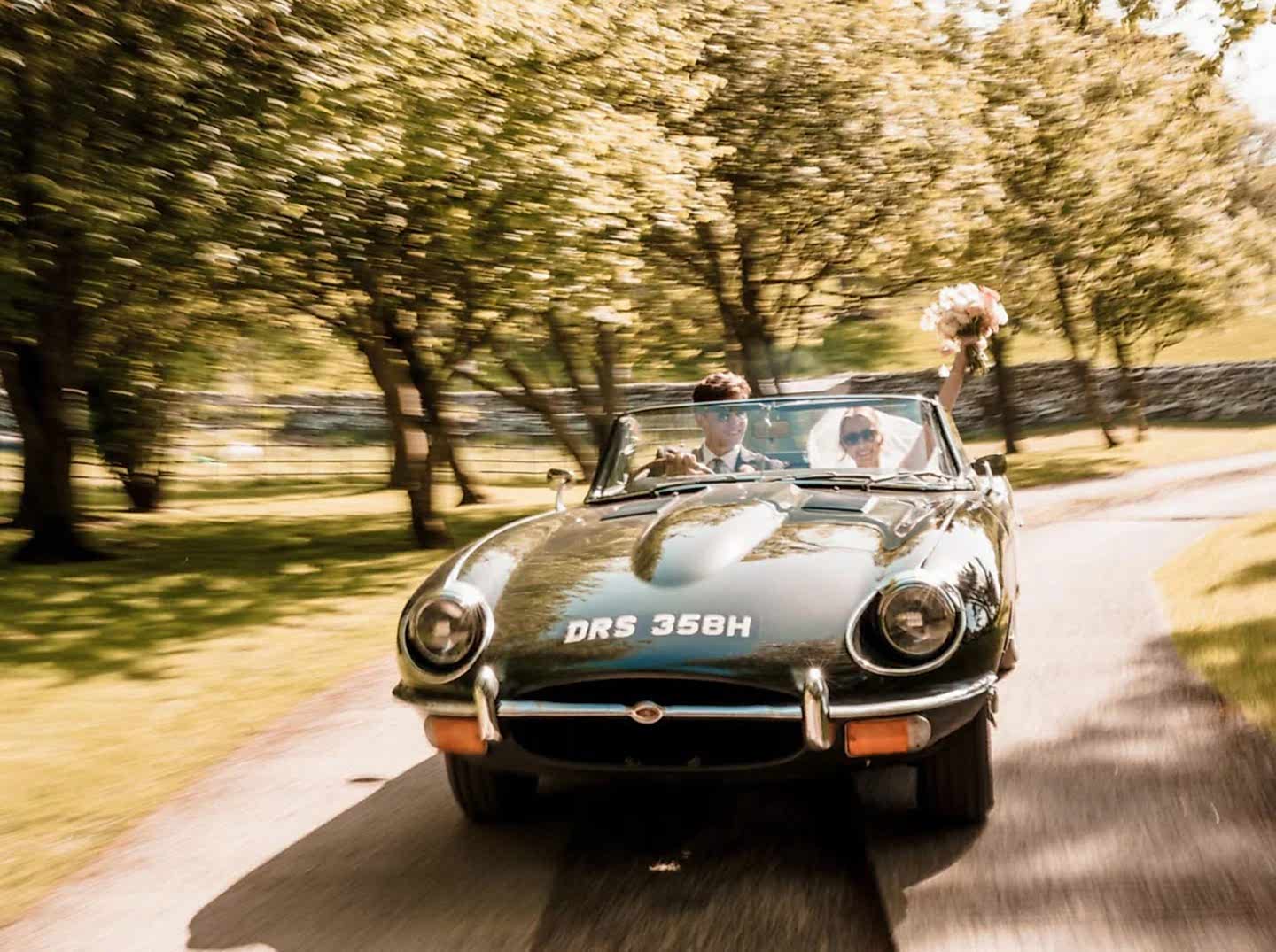 The image shows a Jaguar E Type 4.2 driving through the grounds of Yorebridge House Hotel in North Yorkshire for a spring wedding.