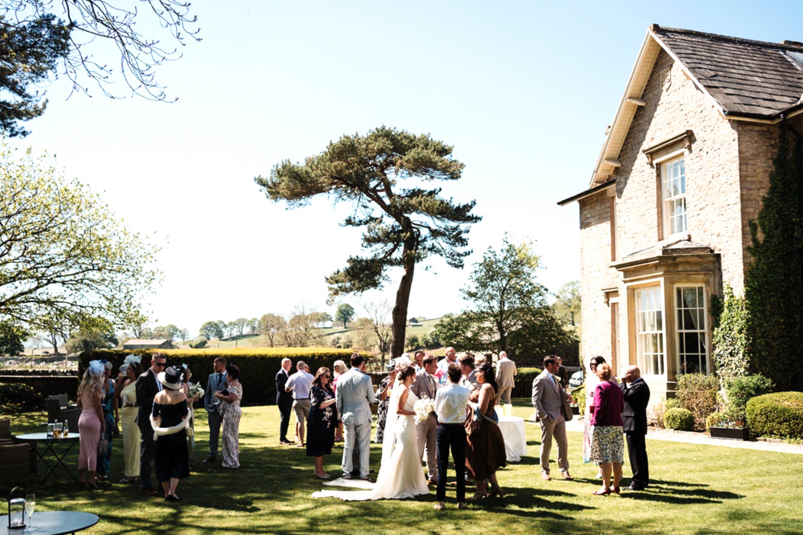 The image shows wedding guests gathered in the grounds of Yorebridge House for an exclusive use house wedding in North Yorkshire.