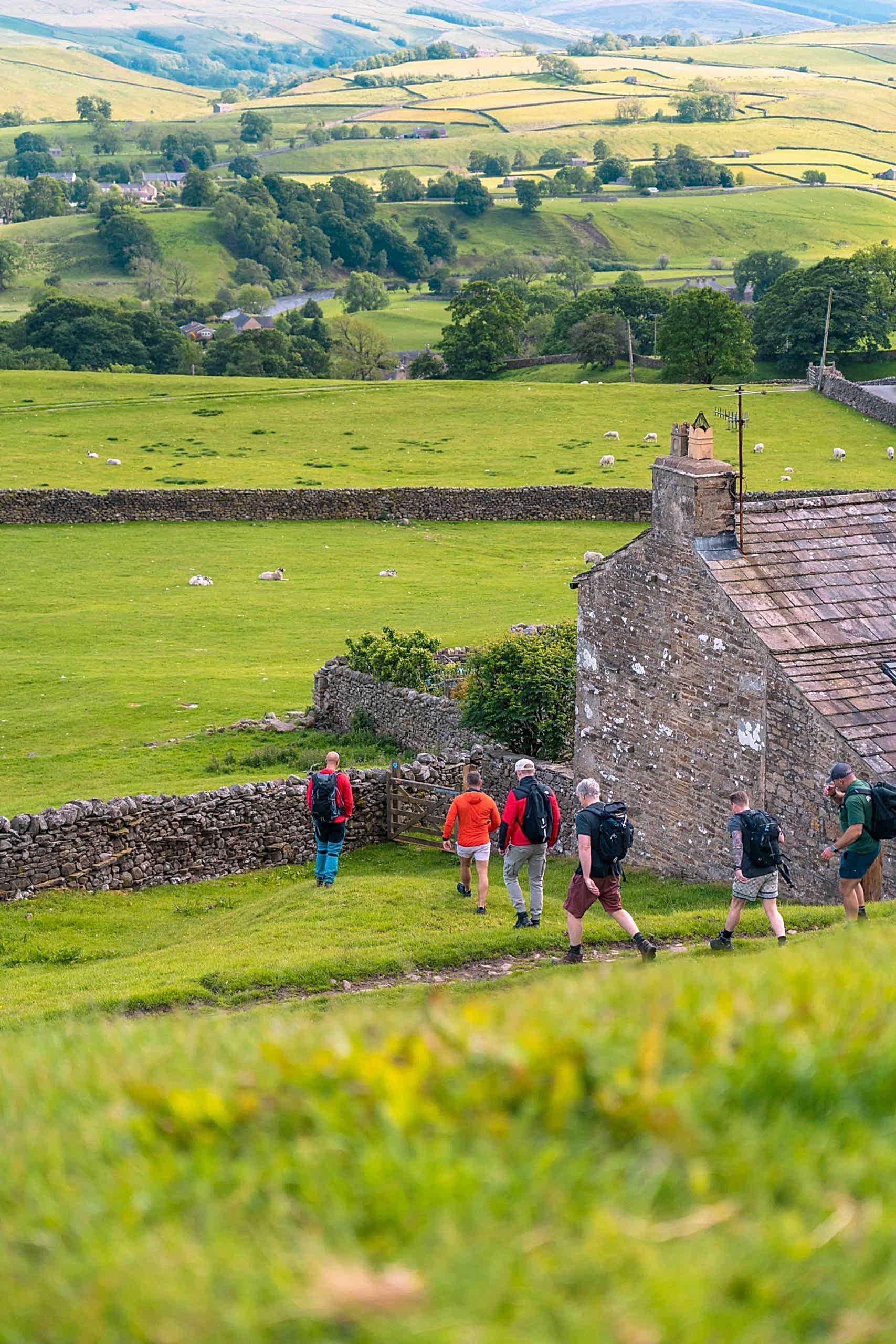 The image shows a group of men hiking in the Yorkshire Dales during a stay at Yorebridge House Hotel in North Yorkshire. Exploring The Dales on foot is the best way to see the sweeping landscapes.