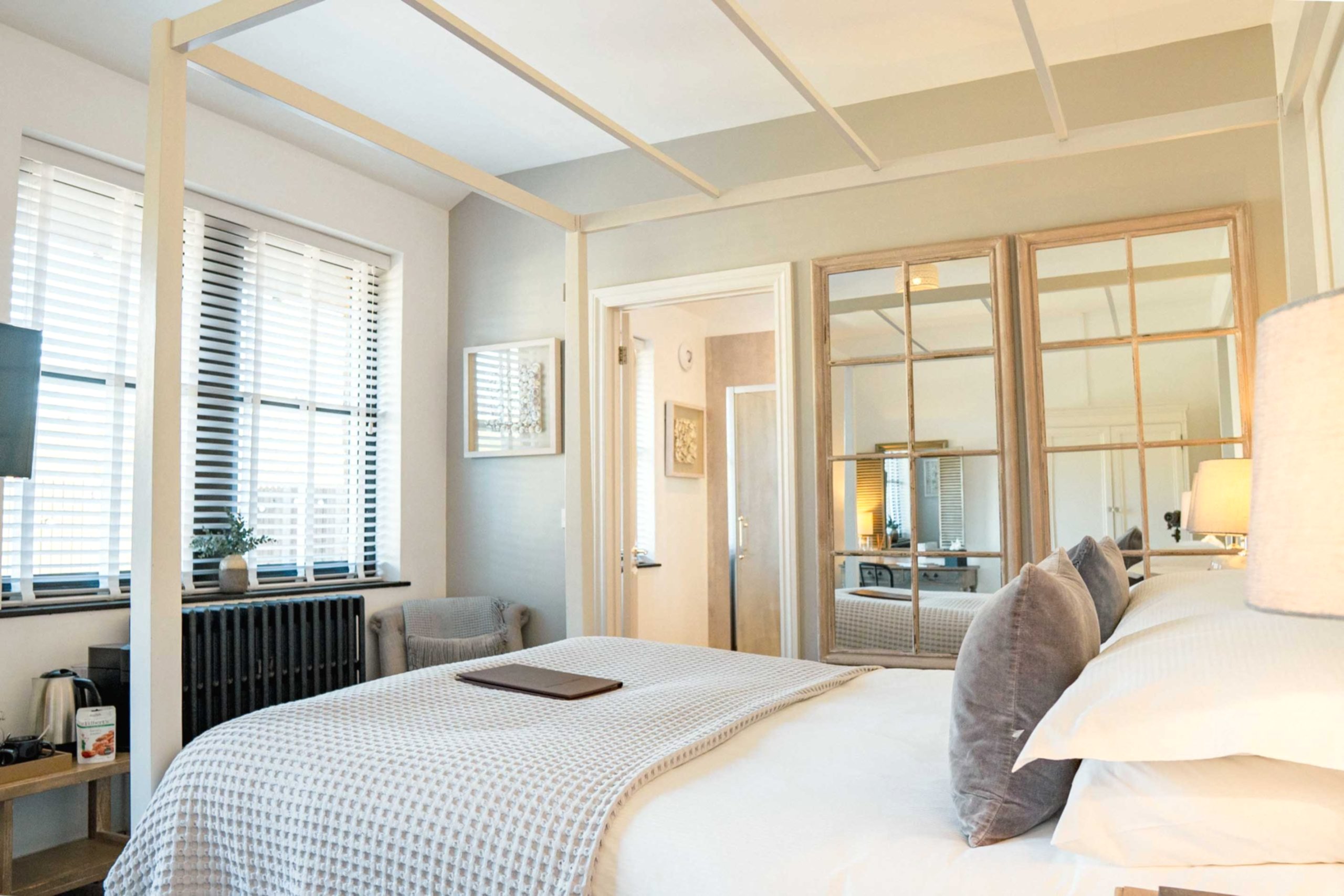 The image shows the four poster bed in the hot tub suite St Jean. This room is a bright and light bedroom in Yorebridge House Hotel in North Yorkshire. The room has its own private terrace, hot tub and rainfall shower, as well as views overlooking the Dales.