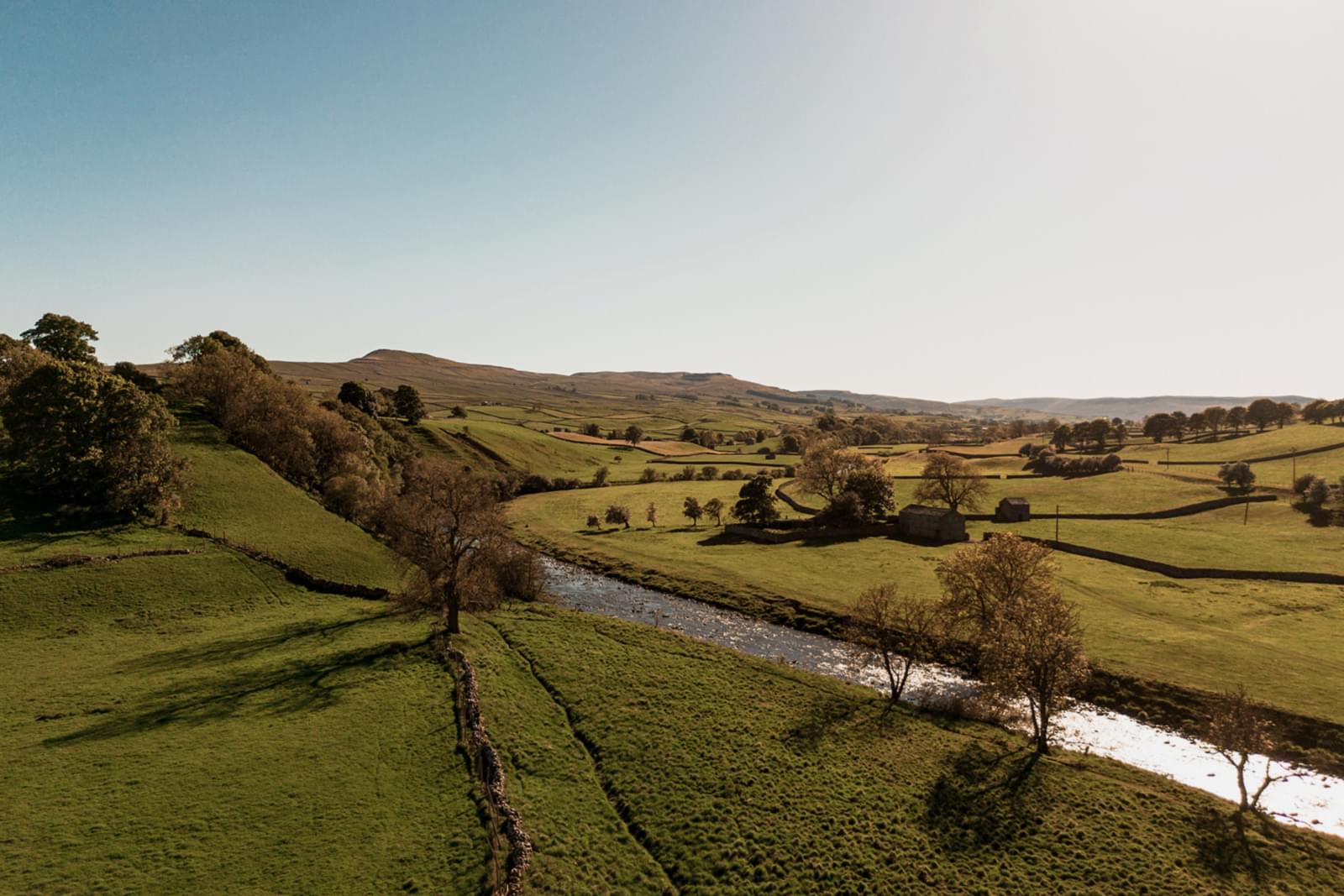 The image shows the Yorkshire Dales countryside from a drone shot. The River Ure runs alongside Yorebridge House Hotel in Bainbridge.